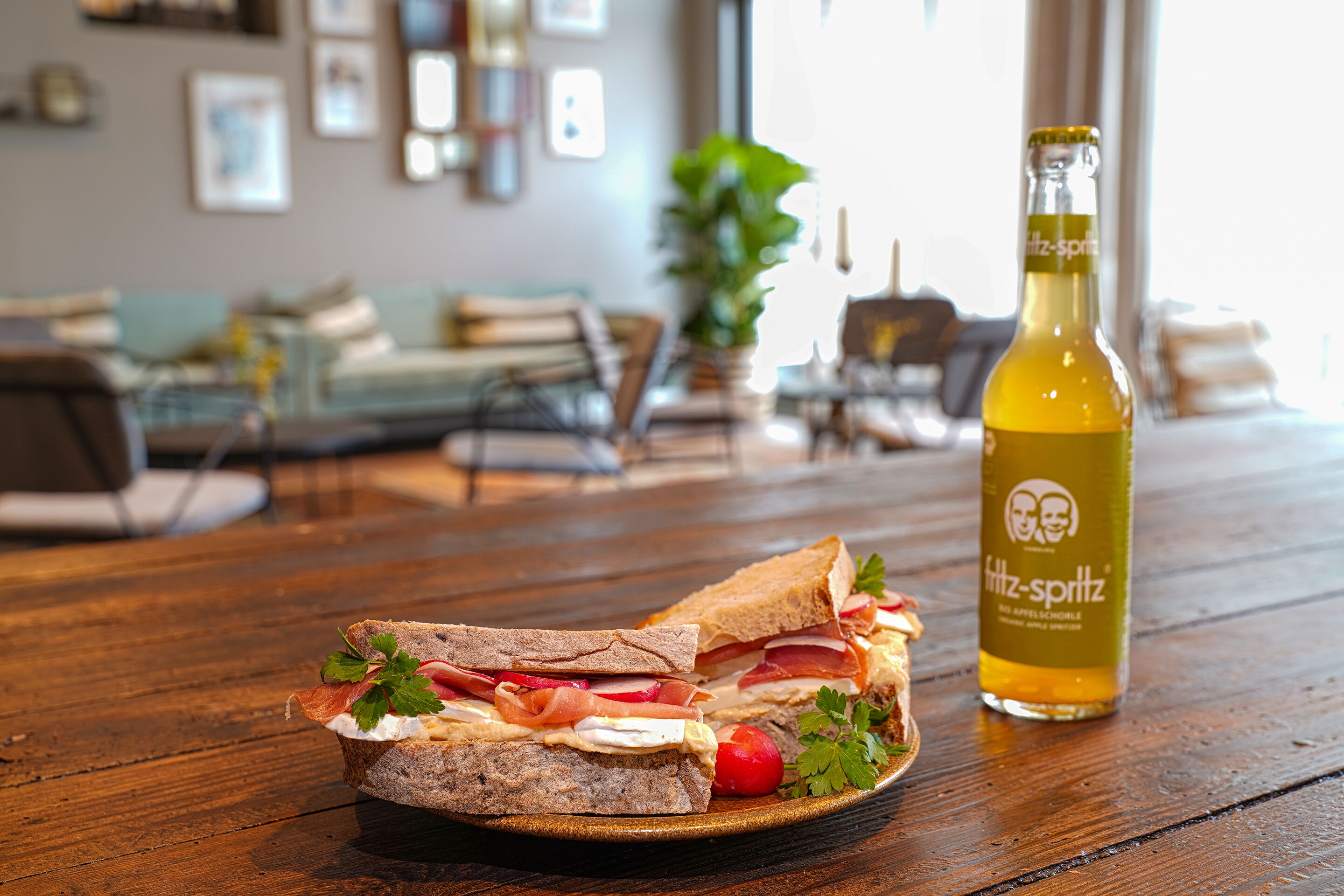 A sandwich on a plate with a bottle of Fritz-Spritz beer on a wooden table.