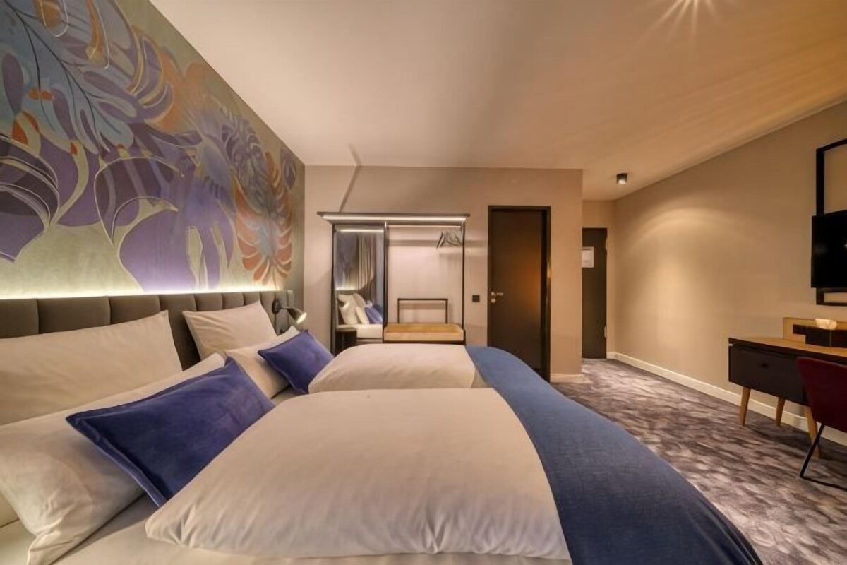 Habitación de hotel con dos camas, un escritorio, una silla, un televisor y un cuadro abstracto grande en la pared.
