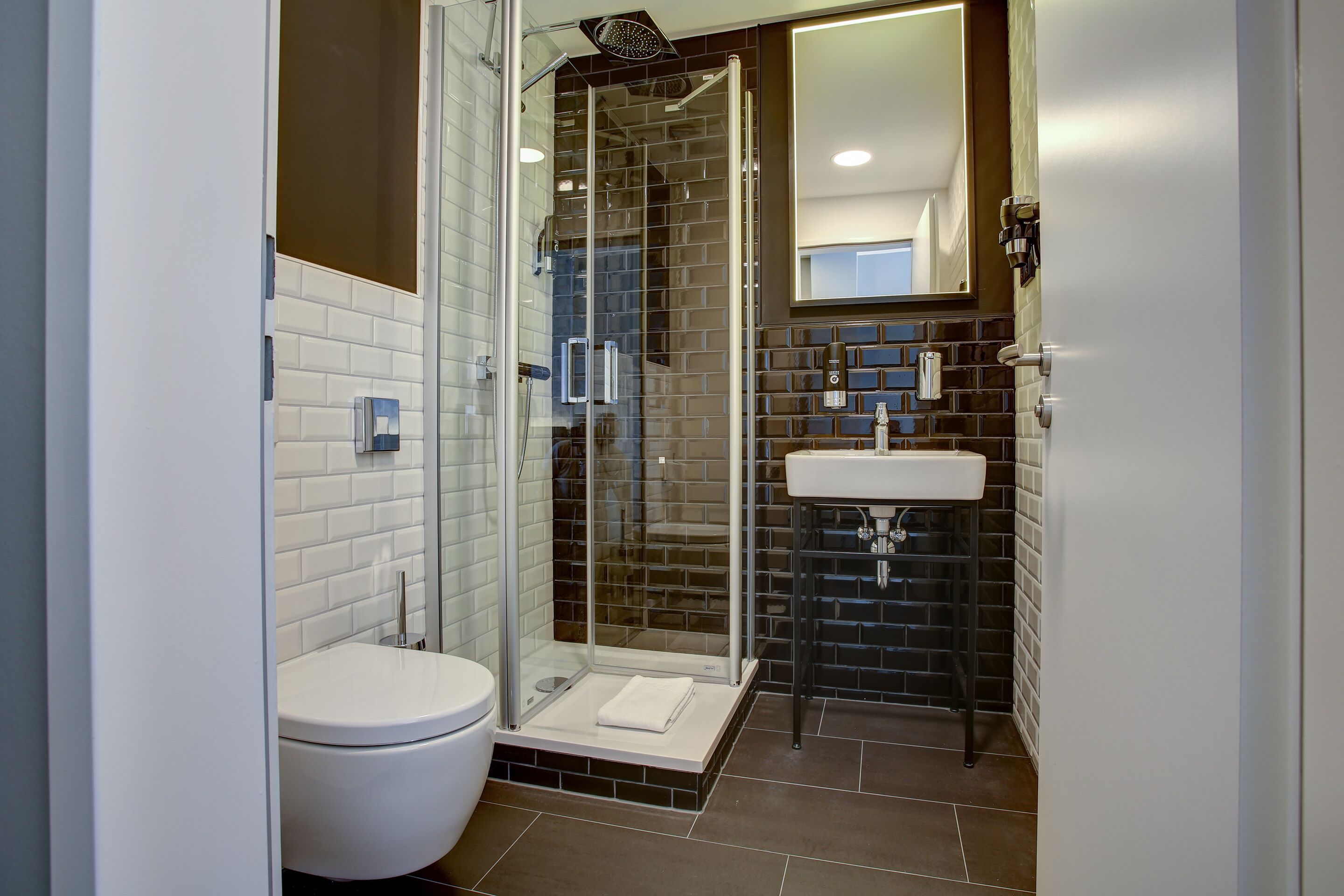 Un baño moderno con ducha envuelta en vidrio, inodoro blanco y lavabo con salpicadero de azulejos.