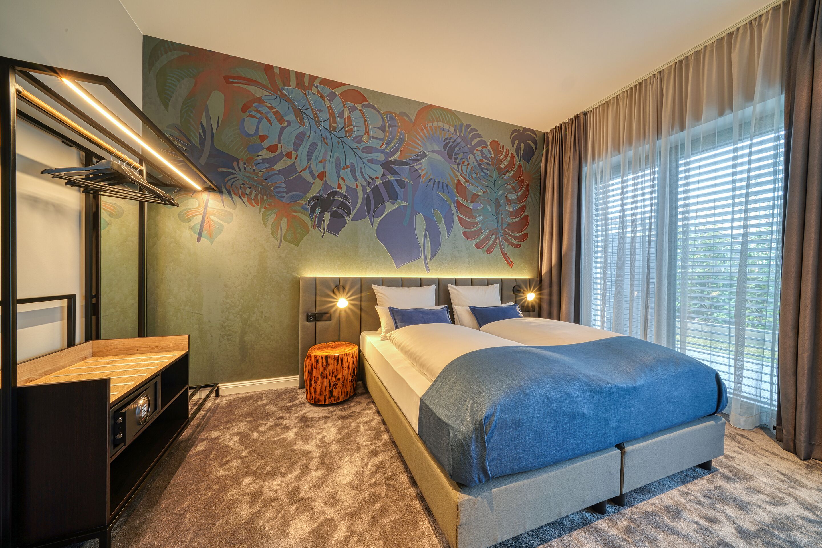 A modern bedroom with a large bed, a side table, a wall-mounted lamp, and a decorative mural.