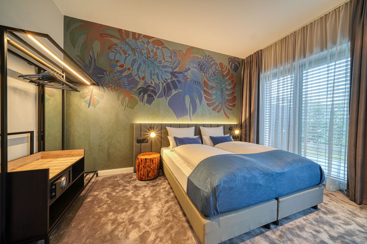 Quarto moderno com uma cama grande, mesa de cabeceira, luminária na parede e um mural decorativo.