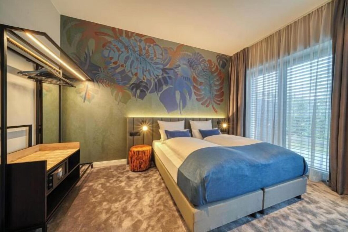 Una habitación de hotel moderna con una cama grande, un escritorio y una lámpara de pared.