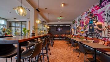 A modern restaurant with a long wooden bar, multiple seating areas, and a vibrant graffiti wall.