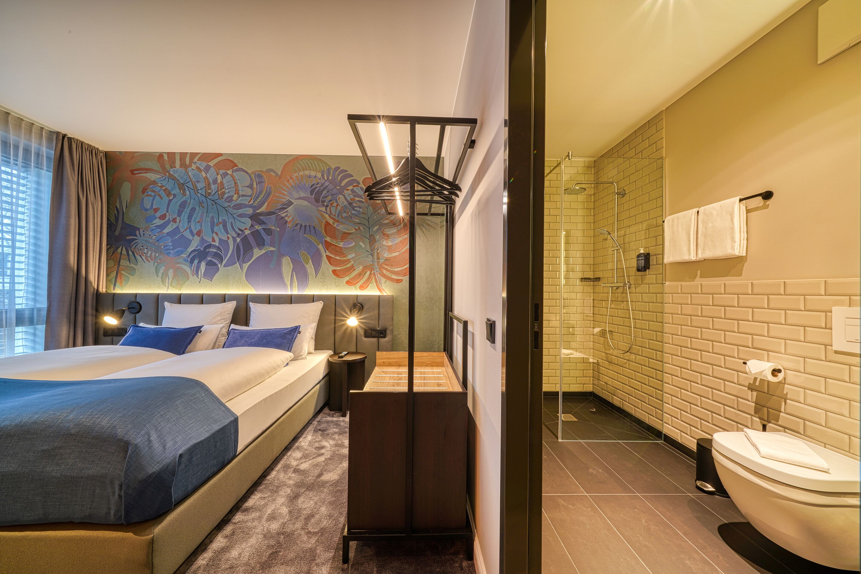 Camera d'albergo moderna con un ampio letto, zona doccia e bagno con WC e lavandino.