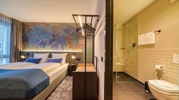 Camera d'albergo moderna con un ampio letto, zona doccia e bagno con WC e lavandino.