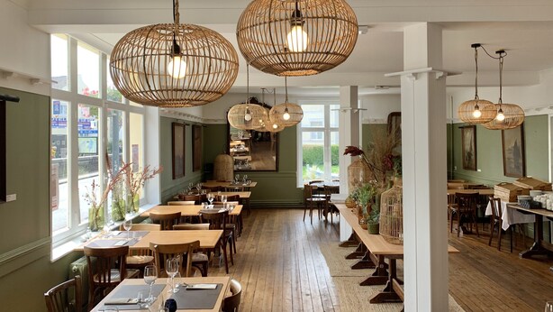 A restaurant with wooden tables and chairs, hanging wicker chandeliers, and large windows with views of greenery. - Hotel de la Plage (Wissant)