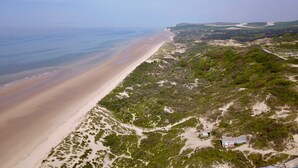 An aerial view of a beach with a sandy shore, green vegetation, and a clear sky. - Hotel de la Plage (Wissant)