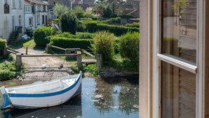 A view from a window overlooking a calm waterway with a small boat docked, surrounded by greenery and traditional buildings. - Hotel de la Plage (Wissant)