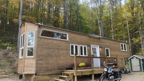 A wooden cabin with a deck, a motorcycle, and a shed in a forest. - Custom-built Tiny House on forested lot near Quechee (Hartland)