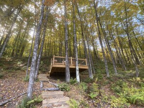 A wooden deck in a forest with a staircase leading up to it. - Custom-built Tiny House on forested lot near Quechee (Hartland)