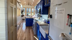 A kitchen with wooden floors, blue cabinets, a white refrigerator, and a ceiling fan. - Custom-built Tiny House on forested lot near Quechee (Hartland)
