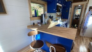 A kitchen with a wooden countertop, two bar stools, and a window with a view of trees. - Custom-built Tiny House on forested lot near Quechee (Hartland)
