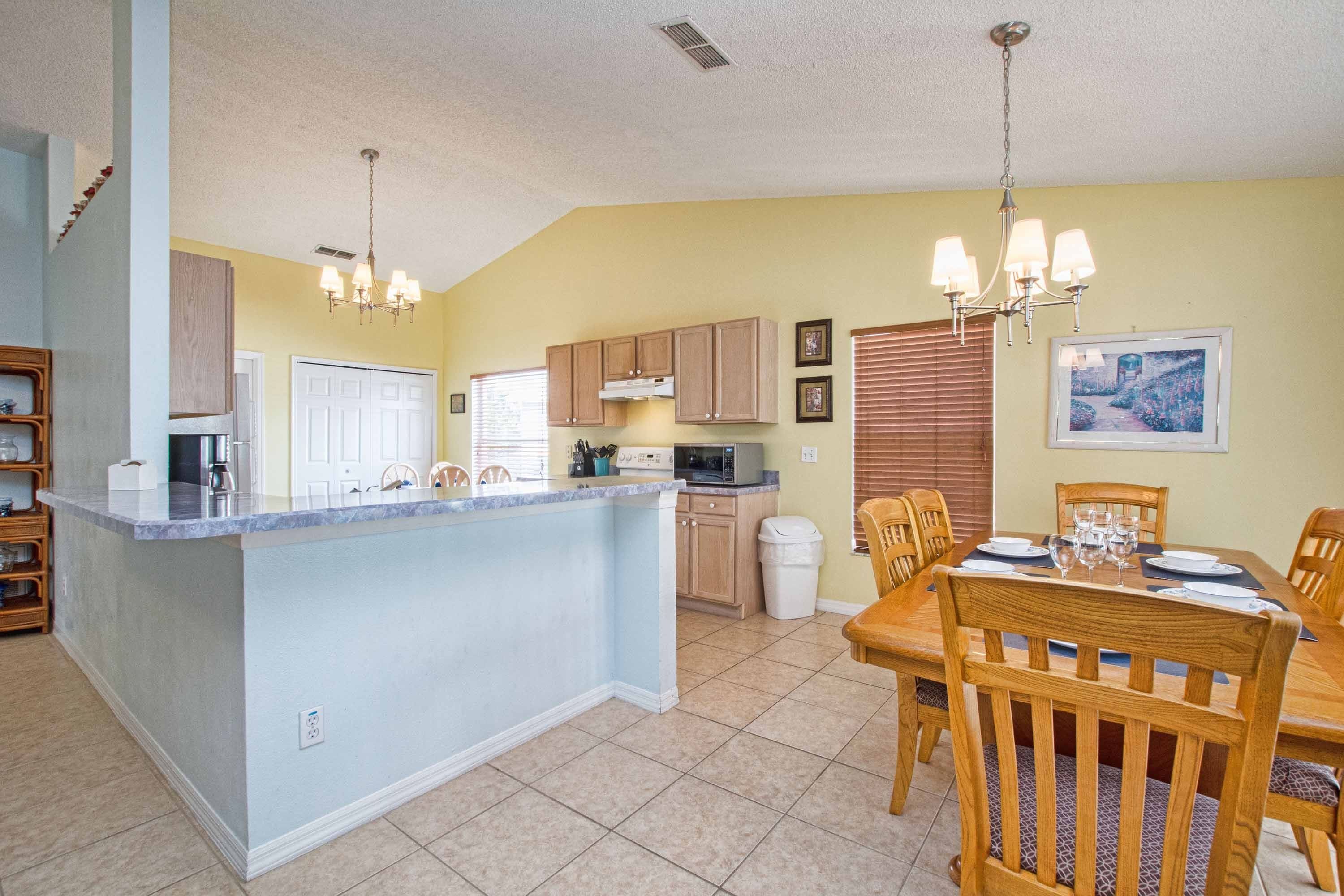A kitchen with a central island, wooden cabinets, a dining table with chairs, and a chandelier.