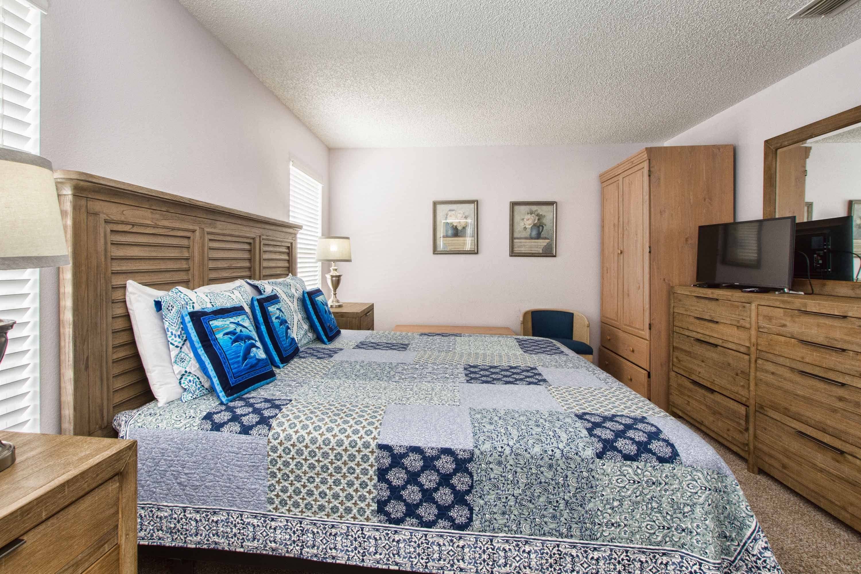 A bedroom with a bed, wooden wardrobe, bedside tables, a television, and two framed pictures on the wall.