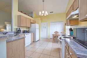 A kitchen with wooden cabinets, a refrigerator, a stove, and a dining area with chairs.