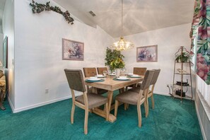 Ein Esszimmer mit Holztisch, vier Stühlen, einer Kristallleuchter und zwei gerahmten Blumenbildern an der Wand.