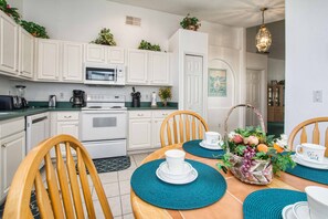 A modern kitchen with white cabinets, a microwave, and a stove. There is a dining table with chairs and a basket of fruit.
