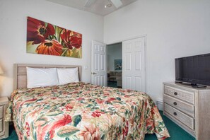 Ein Schlafzimmer mit einem Bett, einem Fernseher, einem Schminktisch und einer Tür zu einem anderen Raum.