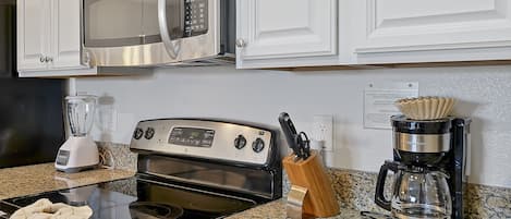 A kitchen with a microwave, stove, blender, and coffee maker.
