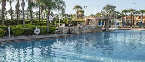 A swimming pool with clear water, surrounded by palm trees and a rock structure.