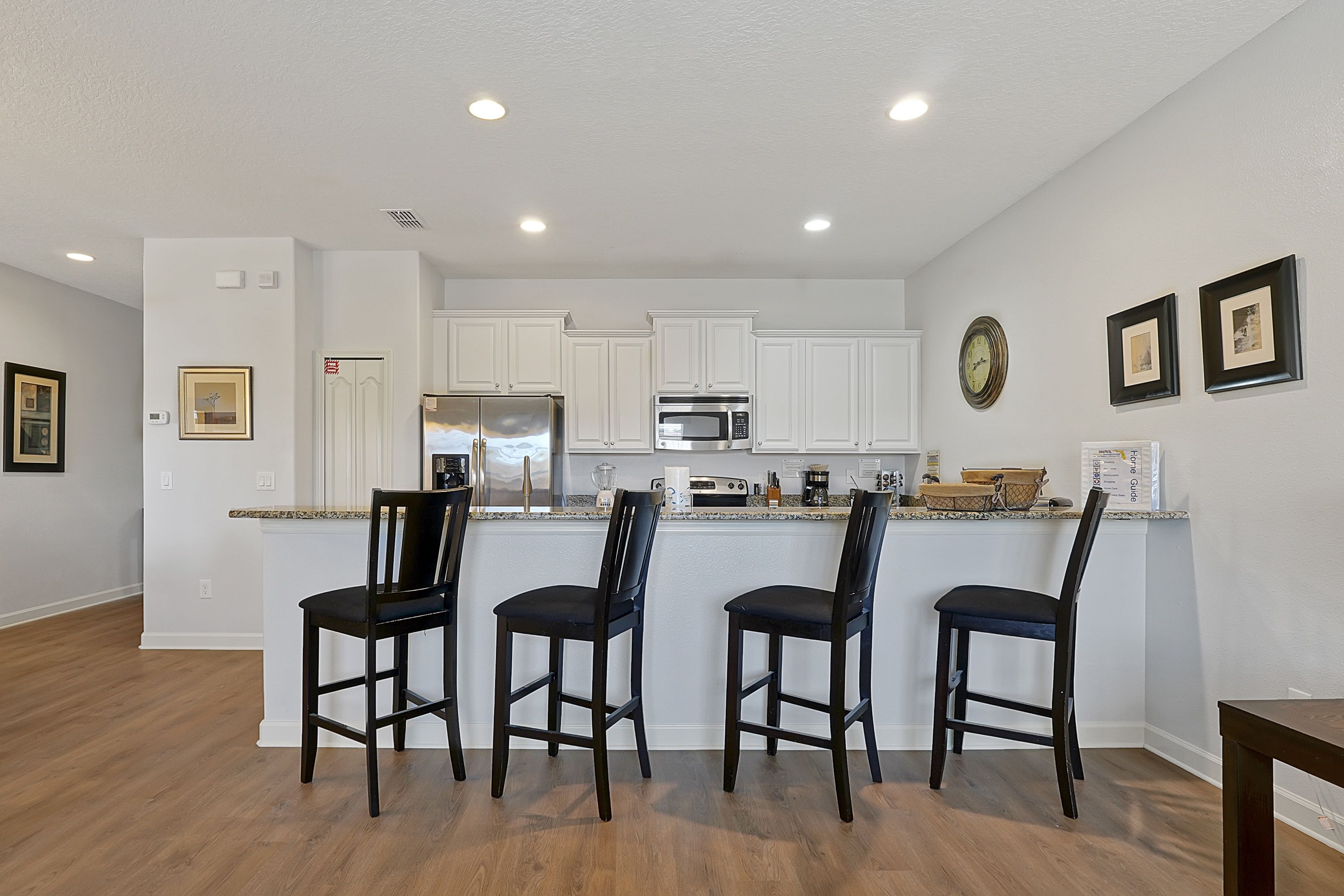 A modern kitchen with white cabinets, stainless steel appliances, and a bar area with four chairs.