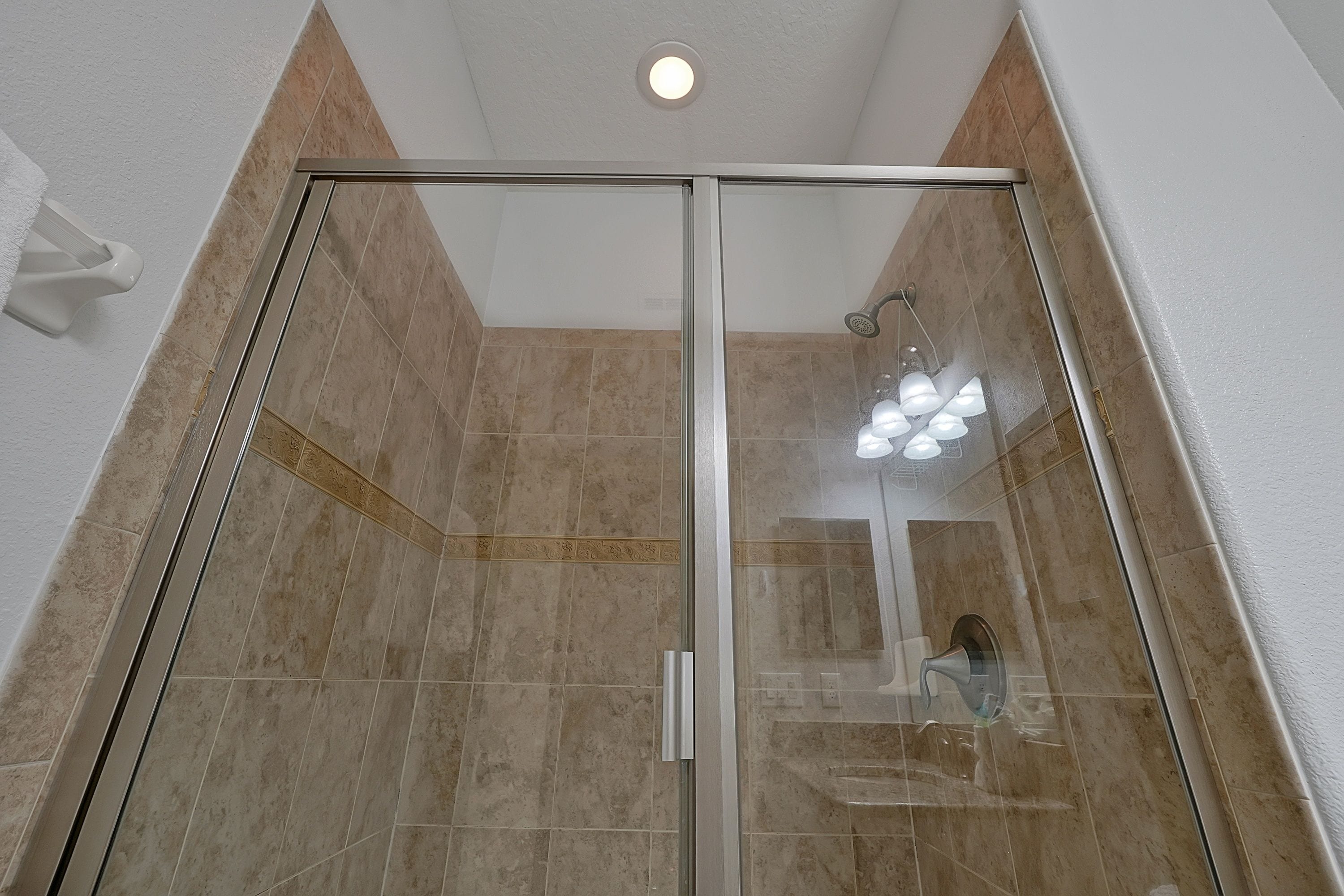 A glass-enclosed shower with a ceiling light and a visible bathroom sink.