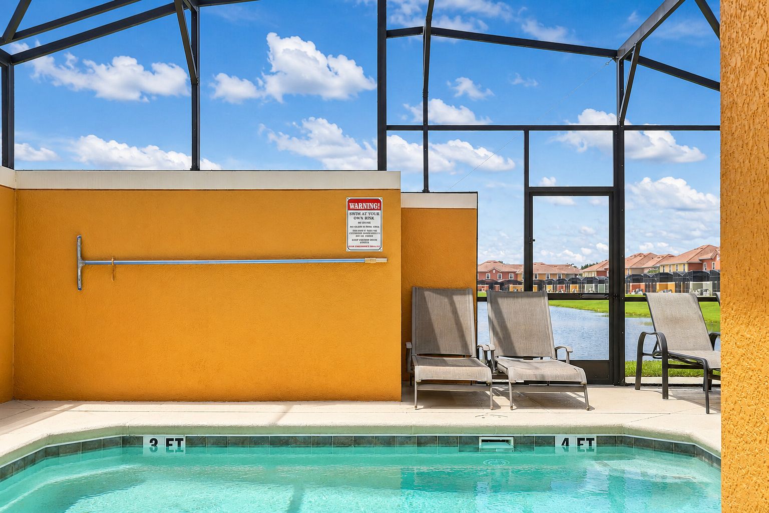 A swimming pool area with lounge chairs, a warning sign, and a view of buildings in the background.