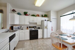 A kitchen with white cabinets, a stove, a microwave, and a refrigerator. There is a dining table with chairs and a window with blinds. - Esprit-3 Bedrooms House w/pool-4100ES 3 Home by RedAwning (Davenport)