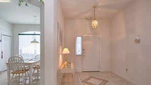 A hallway with a dining area, a lamp, a door, and a patterned floor.