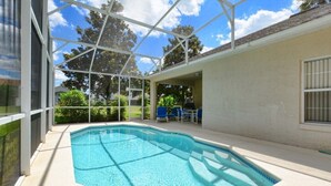 A swimming pool with a glass enclosure, surrounded by a patio area with chairs and a table.