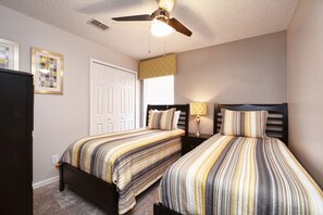 A bedroom with two beds, a ceiling fan, a window with blinds, and a door.