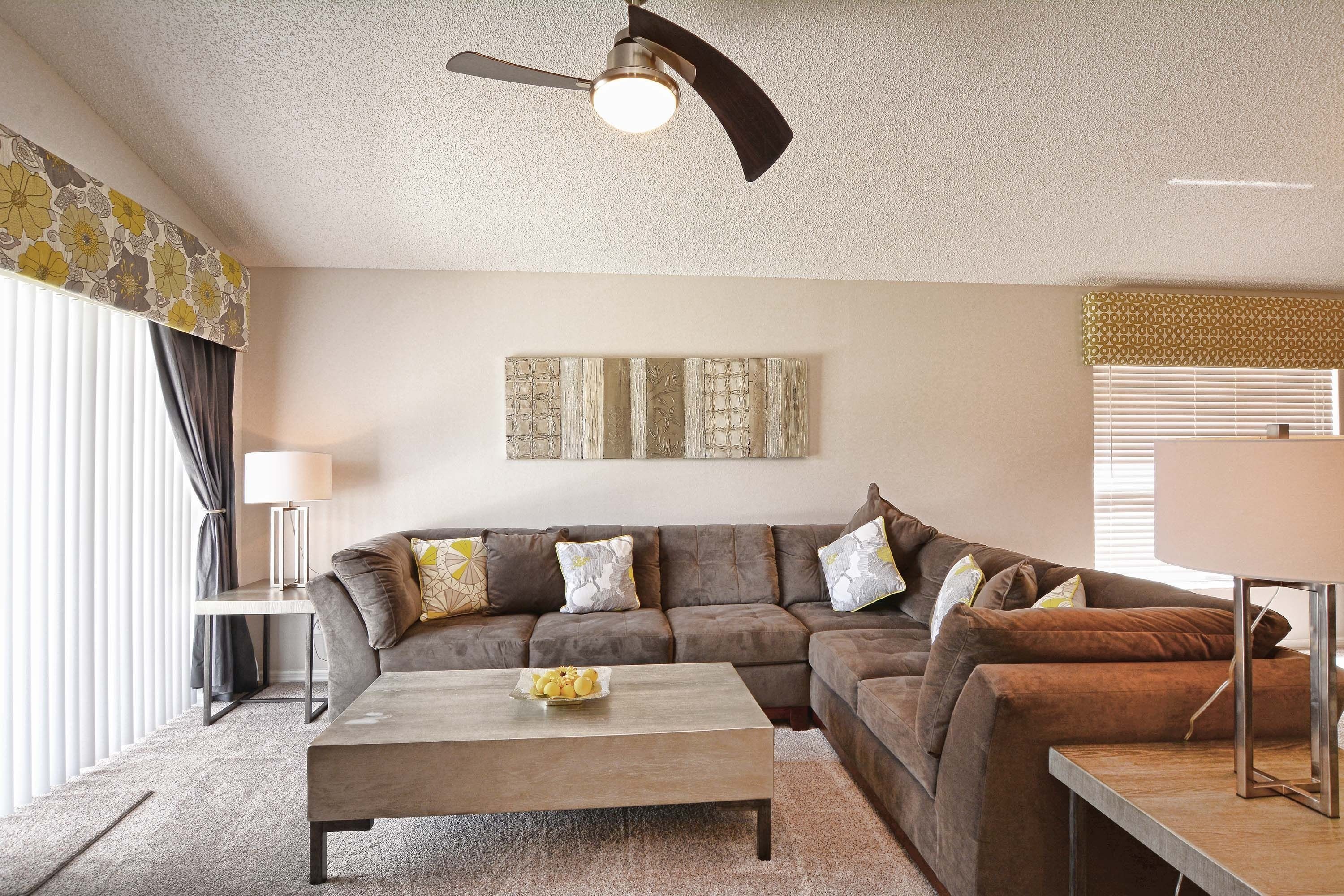 A living room with a sectional sofa, a coffee table, a floor lamp, and a ceiling fan.