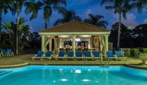 Un espace aménagé au bord de la piscine, comprenant un coin salon couvert et des chaises longues.