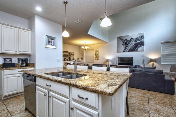 A modern kitchen with granite countertops, a double sink, and white cabinetry.