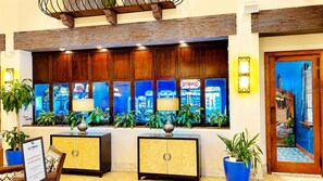 Uma área de recepção com balcão de check-in, plantas em vasos e vista para jogos de fliperama pela janela.