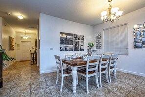 A dining area with a wooden table set for six, white chairs, and a chandelier.