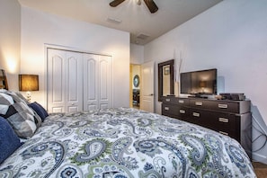 Une chambre à coucher comprenant un lit, une commode, un téléviseur et un ventilateur de plafond.