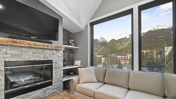 Un salon moderne avec une cheminée en pierre, un canapé beige et une grande fenêtre donnant sur une vue imprenable sur les montagnes.