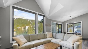 Un salon moderne doté d’un grand canapé d’angle, d’une table basse en bois et offrant une vue sur un paysage montagneux grâce à de grandes fenêtres.