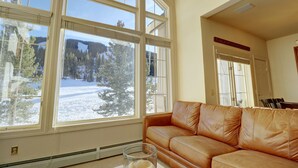 Una sala de estar con un sofá de cuero, ventanas amplias y vistas a un paisaje nevado.