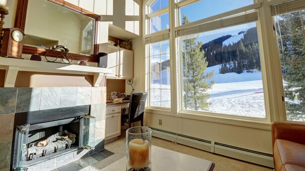 Una habitación con chimenea, un ventanal con vistas a un paisaje nevado y un vaso de bebida sobre la mesa.