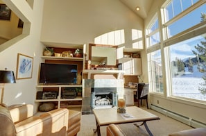 Relax in a cozy seating area with a large flat-screen TV and fireplace, enjoying a scenic view.