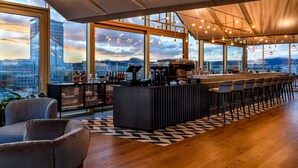A modern bar area with a long counter, bar stools, and a view of the cityscape through large windows. - Radisson RED Hotel, Vienna (Vienna)