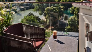 A balcony with wicker chairs, a glass table, and a view of a river and cityscape. - Radisson RED Hotel, Vienna (Vienna)
