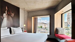 A modern hotel room with a large bed, a red sofa, a view of the city, and a painting on the wall. - Radisson RED Hotel, Vienna (Vienna)
