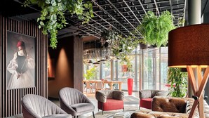 A modern lounge area with comfortable seating, a large window offering a view of the street, and a ceiling with hanging plants. - Radisson RED Hotel, Vienna (Vienna)