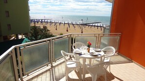 Ein Balkon mit Tisch für Zwei, mit Blick auf einen Strand mit Sonnenschirmen und einem Steg.