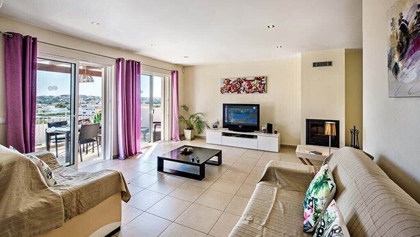 A living room with a TV, sofa, and a balcony with curtains.
