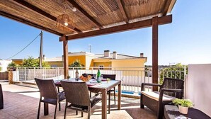 An outdoor patio with wicker furniture, a table with fruits and drinks, and a view of buildings in the background.