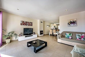 Un salon moderne avec un téléviseur à écran plat, une table basse, un canapé et, au fond, un coin repas.